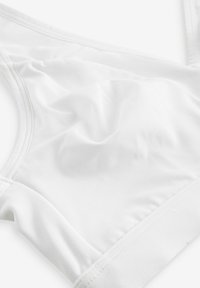 Witte sportbeha van glad materiaal, met een eenvoudig ontwerp, een zachte textuur en een elastische band aan de onderkant voor ondersteuning.