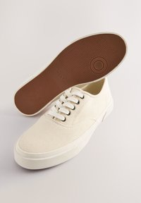 Drobės sportbačiai kremine spalva su šešiais skylučių poromis, baltais raišteliais, apvaliu priekeliu ir tekstūruota šviesiai ruda guma pado dalimi.