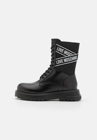 Mustade pahklööbid, millel on sile nahast välimus, nööbid ja tekstuuriga kangas ülemine osa valge "LOVE MOSCHINO" brändimisega.