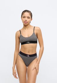 Μπράλετ με ασπρόμαυρο σχέδιο και λεπτές τιράντες, με λωρίδα με λογότυπο, συνδυασμένο με ψηλόμεσο σλιπ με λωρίδα μέσης με λογότυπο.