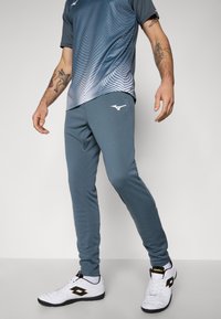 L'ensemble de sport pour homme se compose d'un haut à manches courtes gris et bleu dégradé et d'un pantalon de jogging ajusté assorti. Comprend des chaussures de sport blanches.