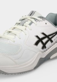Λευκό και γκρι αθλητικό παπούτσι Asics με κορδόνια, μαύρο λογότυπο στο πλάι, υφασμάτινες λεπτομέρειες με υφή και μαξιλαρωτή σόλα σε μονόχρωμο φόντο.