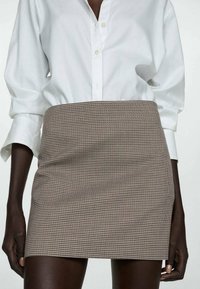 Karierten Minirock aus einer braun- und crèmefarbenen Polyester-Mischung, mit figurbetonter Silhouette und glatter Textur. Kombiniert mit einem weißen Hemd mit Knöpfen.