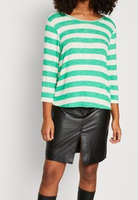 Maglia a maniche lunghe a righe verdi e bianche abbinata a una gonna in pelle nera con spacco frontale, che mette in mostra una texture liscia e un design casual.