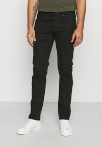 Jeans in denim nero con una vestibilità slim, dotati di cinque tasche, passanti per cintura e chiusura classica con bottone e zip. Indossati con sneakers bianche.