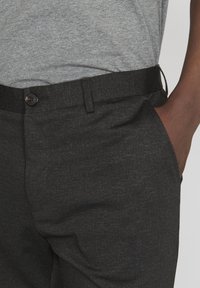 Mörkgrå byxor med en strukturerad yta, med en knappstängning vid midjan och sidofickor. Bärs med en grå t-shirt.