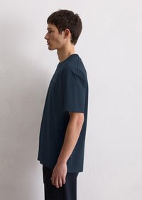 Mørkeblå kortermet T-skjorte med rund hals, laget av bomull. Har et enkelt design med sidespalter og minimalistisk gulltekst på forsiden.