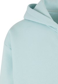 Šviesiai mėlynas gobtuvas su minkšta, lygiame tekstūroje, su laisvu kaklo iškirptės ir pečių siūlėmis, be matomų raštų ar apkaustų.