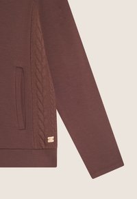 Felpa marrone con pannello laterale a treccia texturizzata, tasca laterale e piccolo logo metallico sull'orlo. Finitura del tessuto liscia.