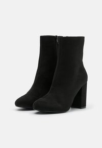 Bottines en suede noir avec un design épuré, bout pointu et talon bloc. Elles sont équipées d'une fermeture éclair sur le côté pour un enfilage facile.