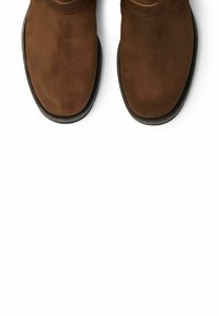 Smeđe nubuk čizme do gležnja s zaobljenim prstima, složenim trakama i kontrastnim šavovima. Ravni crni gumeni potplat s teksturiranim gripom.