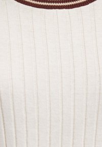 Cremefarbener gerippter Strickstoff mit vertikalen Streifen und einem runden Kragen mit dunkelbraunen und weißen Streifen.