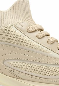 Zapatilla deportiva beige de punto y cuero sintético con cordones a juego, parte superior de tela texturizada y costuras detalladas en el panel lateral y la suela.