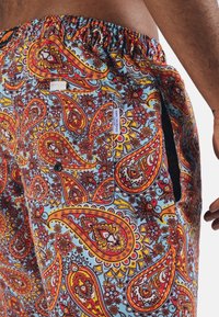 Färgglada paisley-badshorts med en livlig blå bakgrund, mönster i rött och orange, elastisk midja och sidofickdetalj.