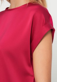 Fuchsia kortärmad skjorta i slät tyg med uppvikt ärm. Har rund halsringning och en figursydd silhuett.