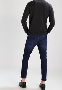 Dark knit sweater, slim-fit dark blue jeans, and black shoes. Visible stitching and back pockets on jeans. Smooth texture overall.