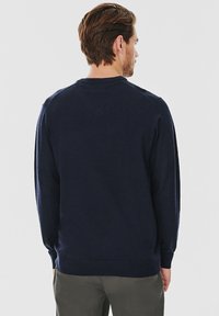 Granatowy pulower z miękkiego materiału, z okrągłym dekoltem, prążkowanymi mankietami oraz prostym, bezszwowym tyłem.