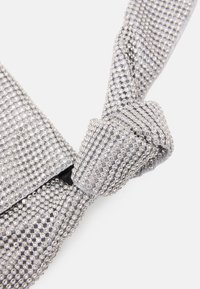 Borsa a rete argentata con design a nodo, decorata con piccole pietre scintillanti, creando una superficie texture e lucida.