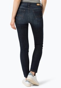 Donker gewassen skinny jeans met een hoge taille, met twee achterzakken en contrasterende stiksels. Gecombineerd met witte sneakers.