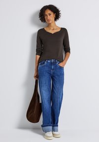 Haut marron à manches longues avec un décolleté en scoop, associé à un jean bleu ample retroussé au niveau des chevilles et des baskets blanches. Sac à main marron.