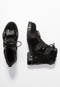 Stivaletti alla caviglia in suede e pelle nera con accenti testurizzati, fibbie, lacci e borchie decorative. Presentano una suola piatta e robusta e una zip.