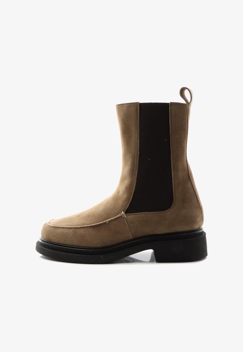 Beige ruskinds ankelstøvle med sorte elastiske sidelapper og en rund tå, suppleret med en kraftig sort sål og en trækstrop.