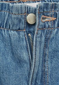 Svijetloplave traperice s patentnim zatvaračem i kopčanjem na gumb, s vidljivim šavovima i glatkom teksturom.