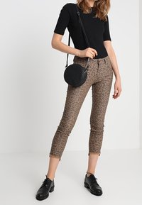Bruna leopardmönstrade skinny jeans med fransar, kombinerat med en svart ribbad kortärmad topp och svarta snörskor. Cirkulär svart väska.