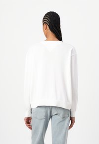 Pull en tricot blanc à coupe décontractée, avec des poignets côtelés et un détail en V dans le dos. Assorti à un jean bleu clair.