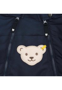 Chaqueta azul marino con cremallera en la parte delantera, que presenta un bordado de la cara de un oso de peluche en el pecho y tiradores de cremallera en forma de oso pequeño.