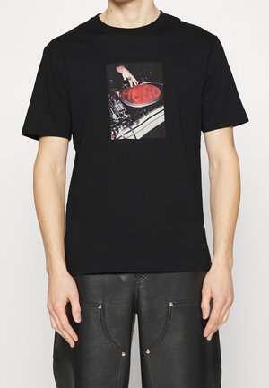 Czarny bawełniany t-shirt z centralnym nadrukiem przedstawiającym rękę na talerzu gramofonu, z czerwonym i białym tekstem. Krótkie rękawy i standardowy krój.