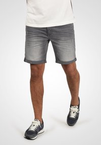 Shorts en denim gris avec une finition délavée, des ourlets roulés et un détail de whiskering subtil. Portés avec des baskets sombres à lacets blancs.