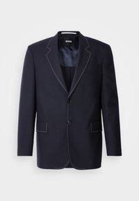 Blazer azul-marinho feito de tecido, apresentando costura branca contrastante ao longo das lapelas e bordas, com dois bolsos frontais e um fecho de botão único.