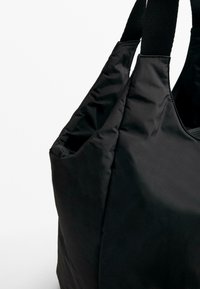 Black fabric tote bag with a soft, textured exterior, featuring wide straps and a slouchy design. No visible hardware or patterns.