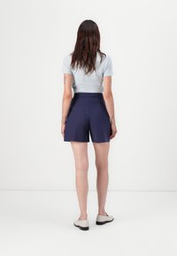 Marinblå högmidjade shorts med skräddarsydd passform, slät front och sidofickor. Kombineras med en ljusblå tät topp och neutrala skor.