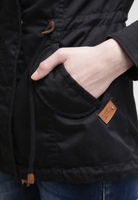 Czarna kurtka z regulowanym paskiem w talii, wyposażona w naszywaną kieszeń, skórzaną metkę oraz gładką, trwałą teksturę tkaniny.