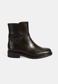 Bottine en cuir marron avec une finition lisse, bout rond et petit talon carré. Présente une sangle décorative avec un détail de boucle.