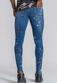 Tunna blåjeans med färgspatter i vitt och rött, med fransar i nederkant och traditionella bakfickor. Tillverkade av denim.