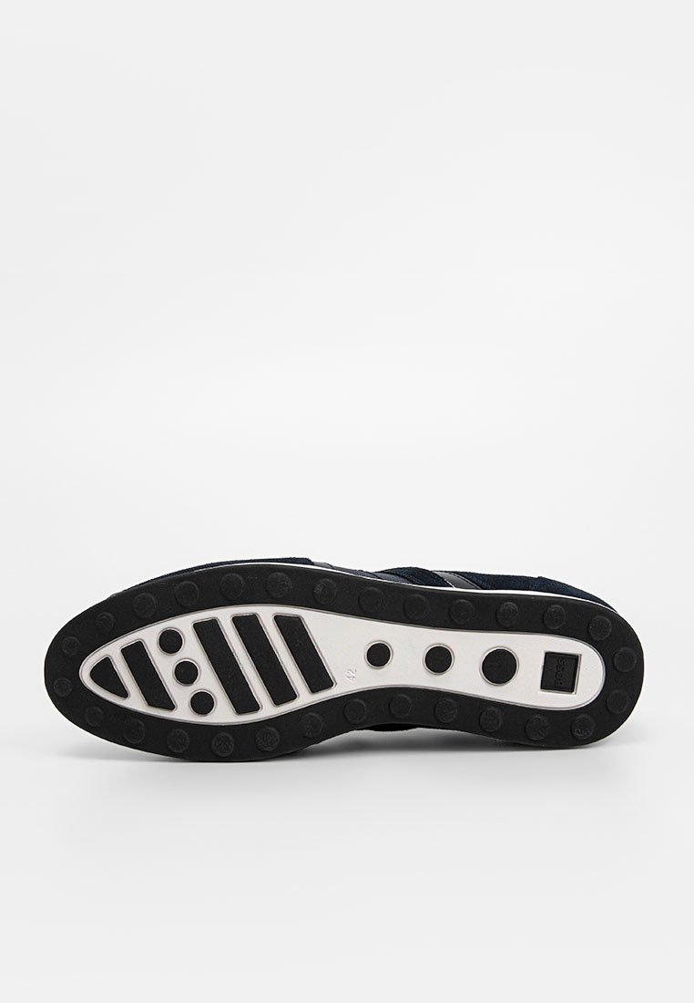 Semelle en caoutchouc noir avec des motifs circulaires, dotée d'une semelle intermédiaire blanche et d'une surface texturée. Les accents latéraux incluent des rayures horizontales. Taille 42.