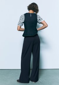 Spijkerjasje met een aansluitend ontwerp, marineblauwe kleur en ritssluiting aan de achterkant, gecombineerd met een gestreept T-shirt met korte mouwen en zwarte broek met wijde pijpen.