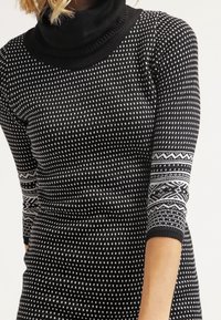 Maglione nero lavorato a maglia con colletto alto, caratterizzato da un motivo geometrico bianco e polsini a fantasia in contrasto. Texture morbida e design aderente.