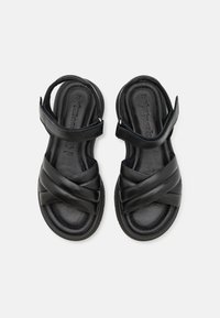 Sandales en cuir noir avec des lanières entrecroisées et des brides de cheville réglables. Semelle intérieure rembourrée et semelle texturée pour plus de confort.