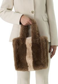 Faux fur tote bag met donkere bruin en lichtbeige panelen, fluffy textuur, dubbele handvatten en een gouden accent.