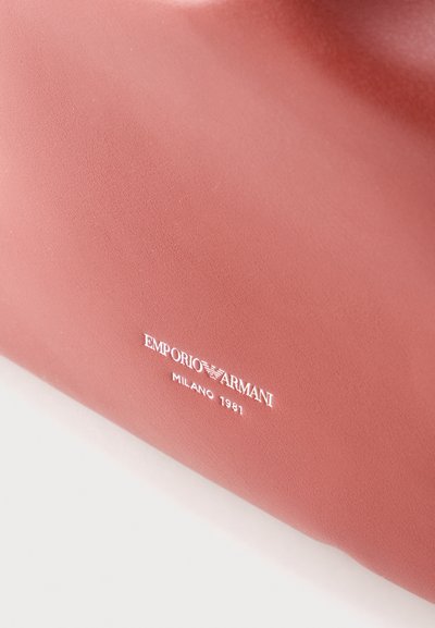 Gros plan sur un article Emporio Armani lisse et rose poudré avec un texte de logo blanc indiquant "EMPORIO ARMANI MILANO 1981".