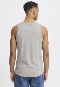 Camiseta sin mangas gris de algodón con dobladillo redondeado y amplias sisas, vista desde atrás. Combinada con pantalones cortos de mezclilla azules.