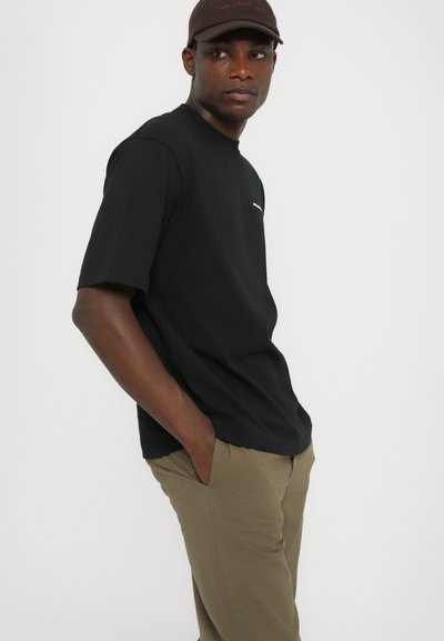 Tricou negru din bumbac, cu mâneci scurte, croi lejer și un mic logo alb pe pieptul stâng. Asortat cu pantaloni verzi măslin.