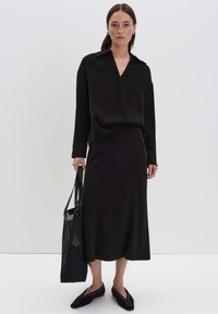Blouse noire décontractée à manches longues avec un col en V, associée à une jupe midi assortie. Comprend des chaussures plates et un sac fourre-tout en maille noire.