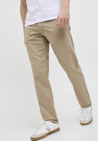 Khakinväriset puuvillahousut, joissa on rento istuvuus, suorat lahkeet ja hienovaraiset ompeluyksityiskohdat, yhdistettynä valkoisiin tennareihin, joissa on vaaleanharmaat korostukset.