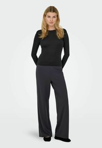 Svart langermet topp med bølget halslinning, kombinert med høytlivs vide bukser i mørkegrått. Mykt, glatt stoff med en avslappet passform.
