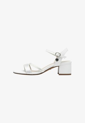 White heeled sandals with a block heel, featuring adjustable ankle straps, cross-over metallic and matte straps, and a smooth sole.